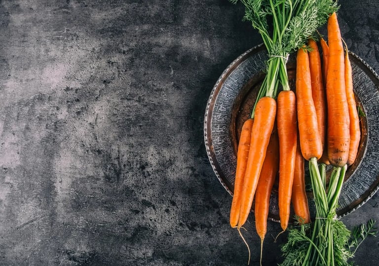 Des carottes dans une vieille assiette en fer avec un fond gris foncé.