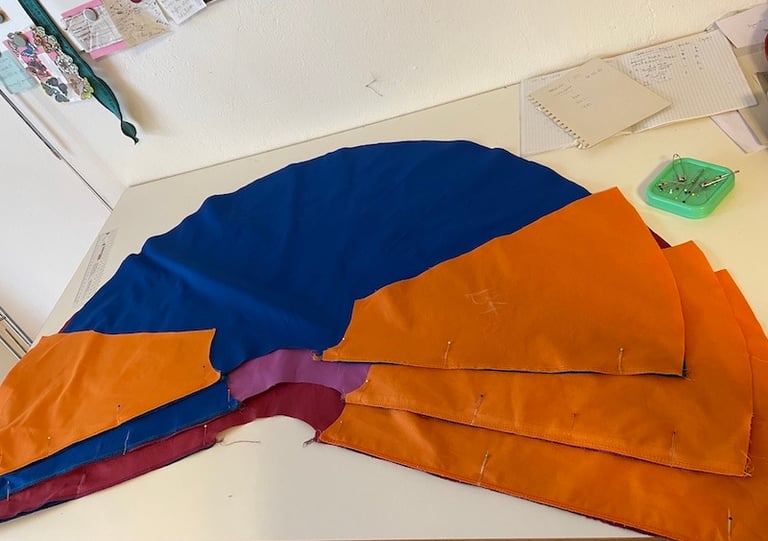A colorful fabric pattern for a cape pinned and laid out on a white sewing table.