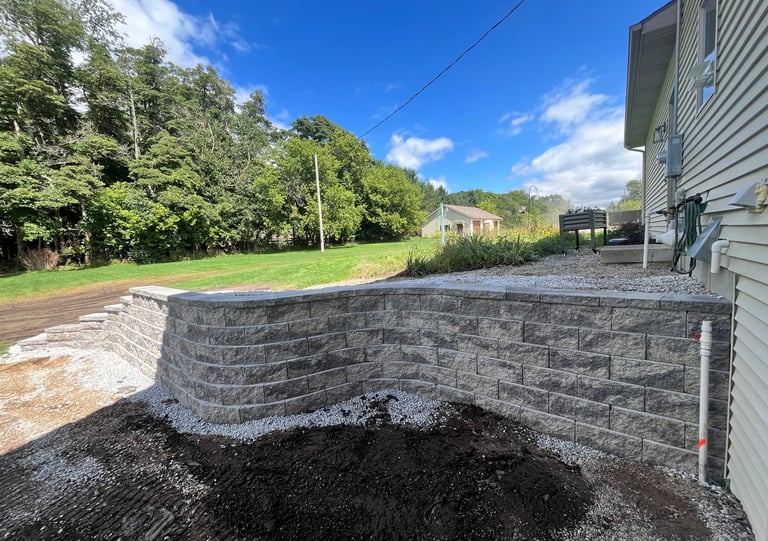 Newly installed grey stone retaining wall in a residential backyard with landscaping and green lawn.