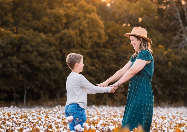 Mom laughing and holding her son's hands in a cotton field during the evening golden hour. 
