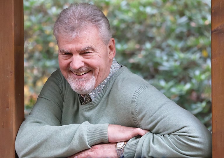 Willem lacht open en vriendelijk terwijl hij ontspannen leunt in een houten raamkozijn, omgeven door