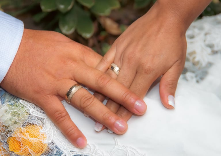 Primer plano de las manos de una pareja casada mostrando anillos de boda de oro sobre un vestido de 