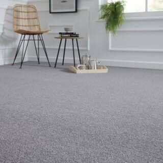 Plush grey textured carpet in a modern living room with a wicker chair and side table.