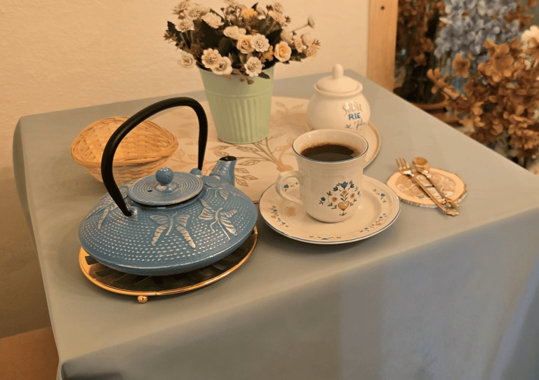 Vintage blue cast iron teapot and floral ceramic coffee cup on a table with flowers.