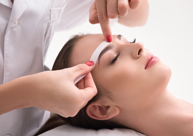 a woman getting a facial wax from a woman in a white shirt in a salon 
