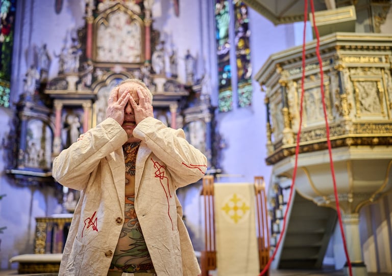 Ein Schauspieler in einer Kirche. Er verdeckt sein Gesicht mit den Händen.