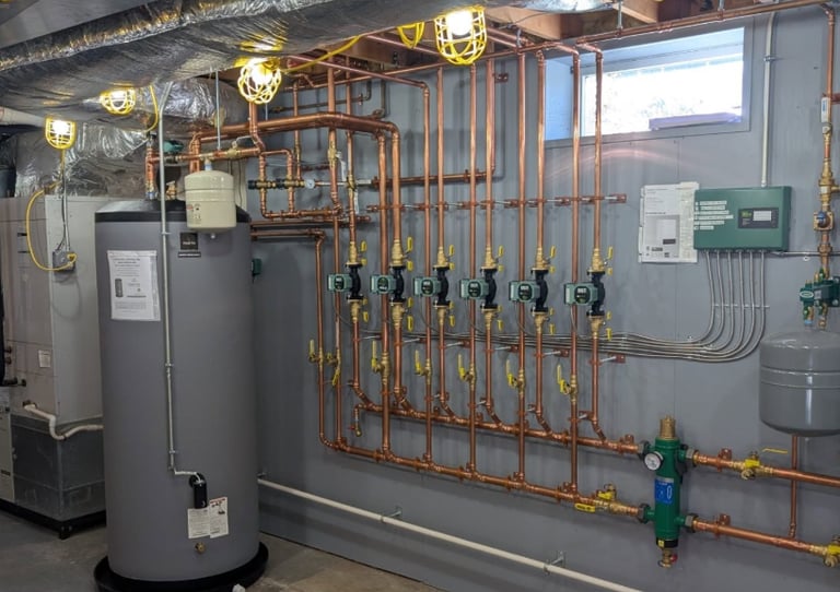 Professional basement boiler installation with copper piping, circulator pumps, and water storage tank.