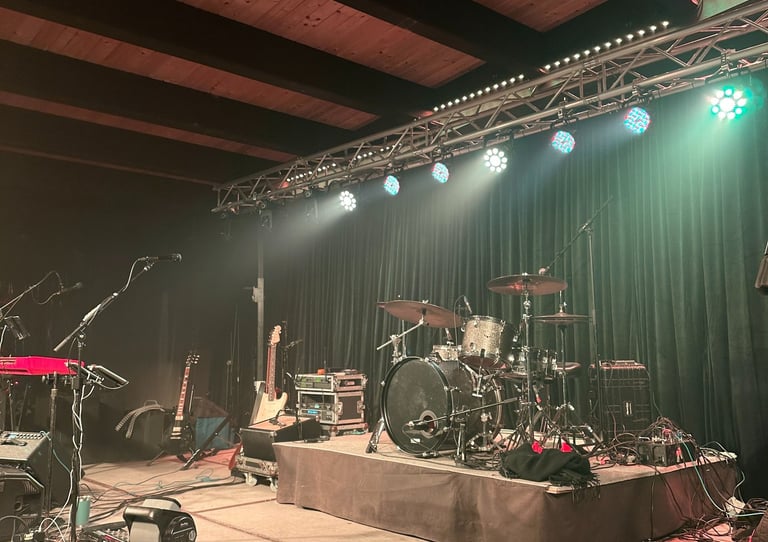 Live music stage setup with a drum kit, electric guitars, and professional concert lighting.