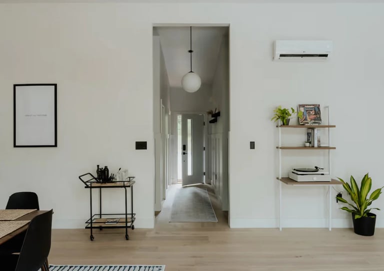 a room with a table and chairs and open front door looking down hall