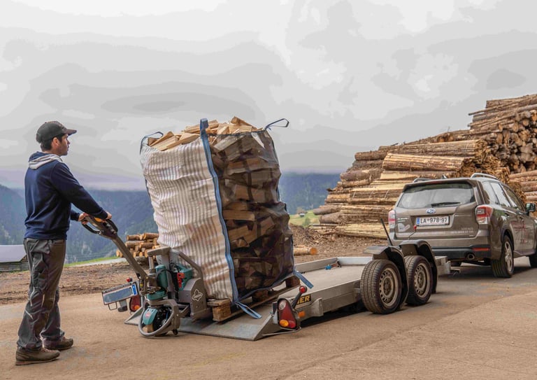 ein mitarbeiter fährt ein Big Bag voll mit brennholz auf einen Autoanhänger um ihn auszuliefern