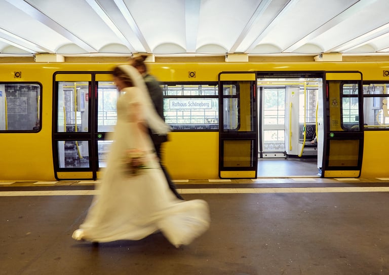 Braut und Bräutigam gehen an einer U-Bahn vorbei in Berlin.