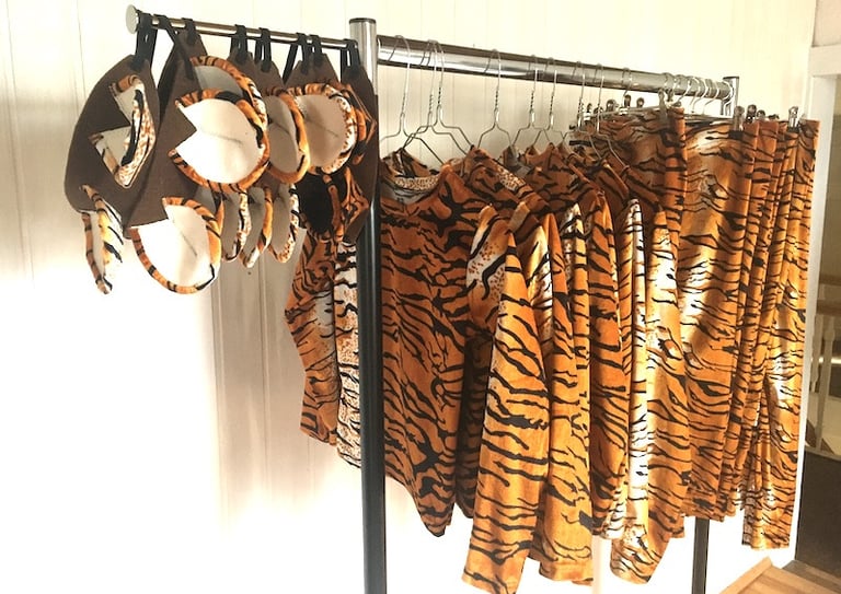 Tiger print costume sets including shirts, leggings, and ears hanging on a garment rack.