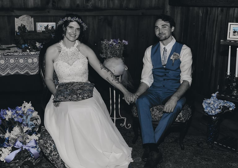 a bride in a white dress and a groom in a blue suit holding hands and sitting in a decorated barn