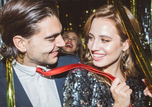Smiling young couple celebrating a New Year's Eve party with gold tinsel and sequins.