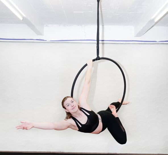 Vrouw in zwarte outfit voert een aerial hoop oefening uit bij De Polecats Fabriek in Gent