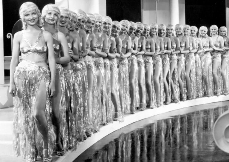 Line of Whoopee! (1930) chorus girls in gold lamé and blonde wigs standing beside a reflecting pool.