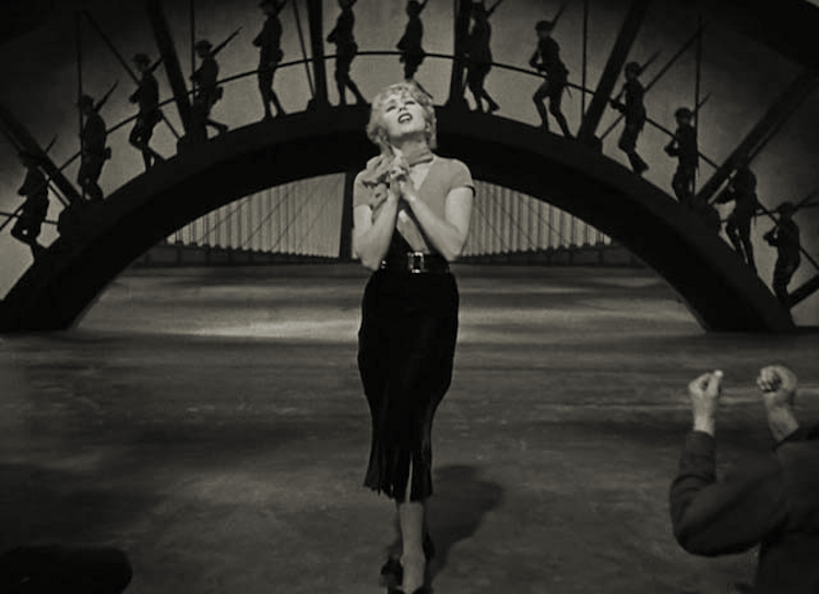 Joan Blondell singing “Remember My Forgotten Man” with WWI soldiers on a semi‑circular bridge behind