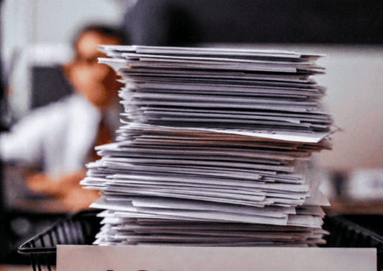 Una pila alta de documentos aprobados en una bandeja etiquetada como ACEPTADO