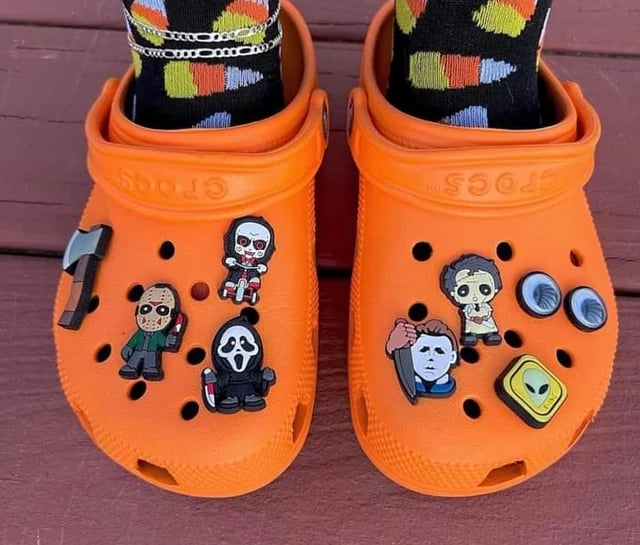 a person wearing orange crocs with halloween charms