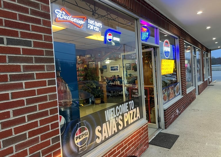 Exterior of Sava's Pizza storefront with neon beer signs and Pepsi logo on a brick building.
