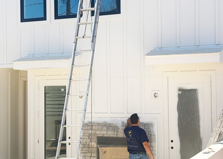 Professional painter prepping a white board and batten home exterior for modern house siding repair.