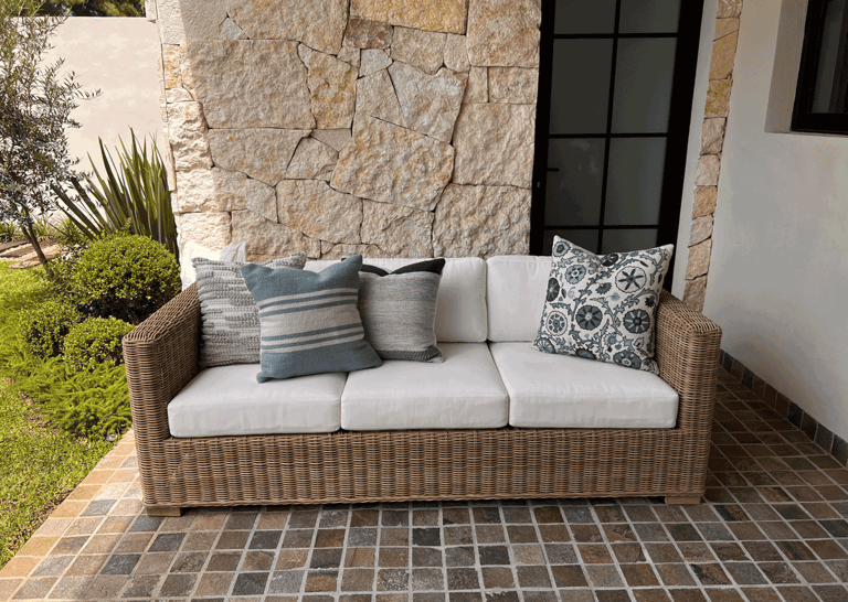 Terraza con sofá tejido, cojines decorativos y muro de piedra natural con vegetación | KARÄNA
