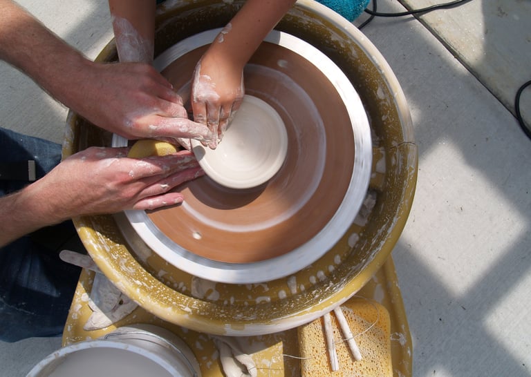 Two hands forming a ceramic bowl on a potter's wheel.