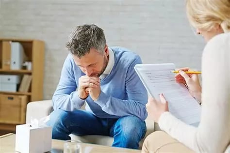 Femme aidante écoute un homme penché en avant coudes sur ses cuisses