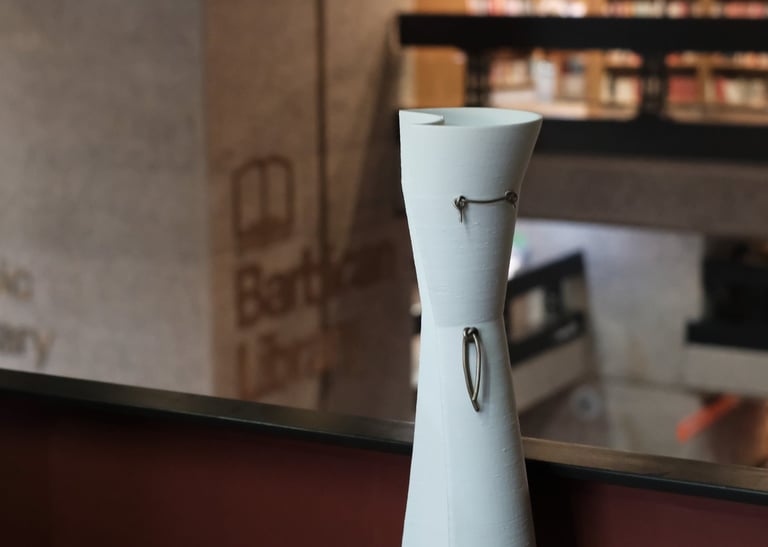 A tall elegant white porcelain vessel, with bronze knot details, on a shelf in the Barbican Library