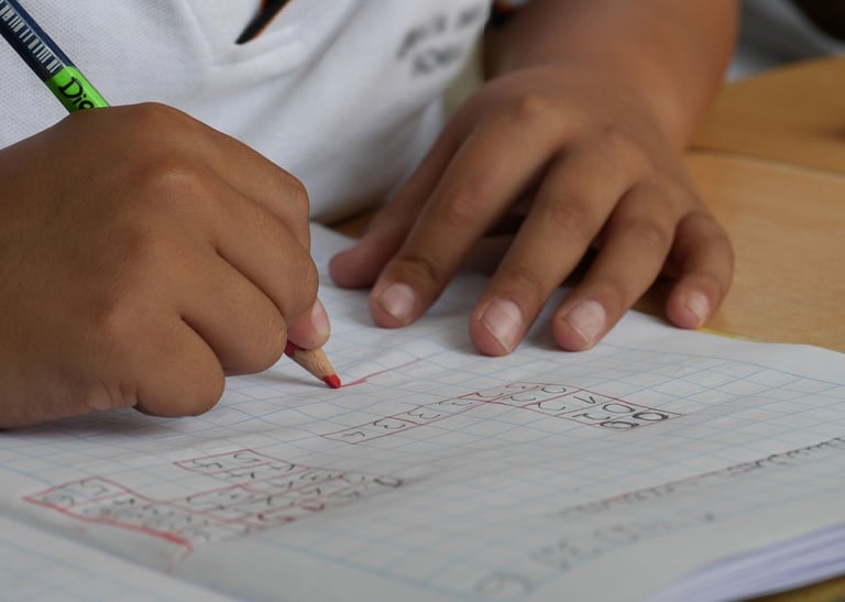 Two young, brown hands on paper, the right one writing with a colored pencil