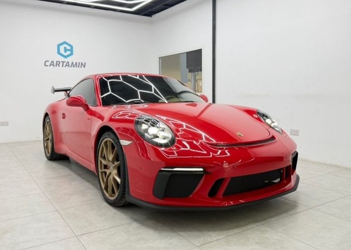 Red Porsche 911 GT3 luxury sports car with gold wheels in a showroom.
