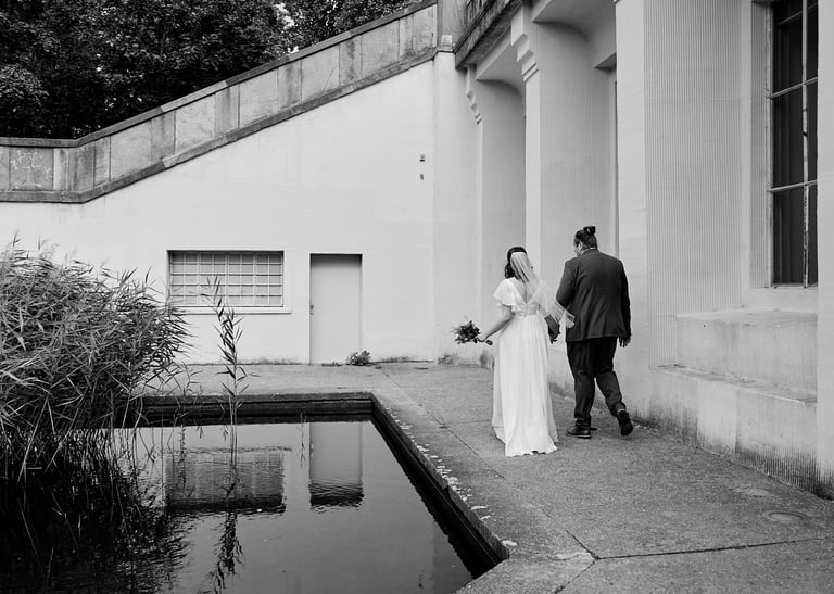 Newlyweds walking along a pond in a park.
