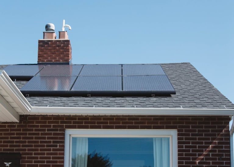 Modern solar panels installed on a residential dark shingle roof of a brick house.