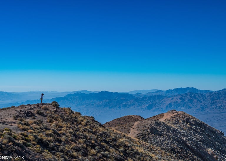 a man overlooking dantes peak with more hazy mountains in the distance in death valley california