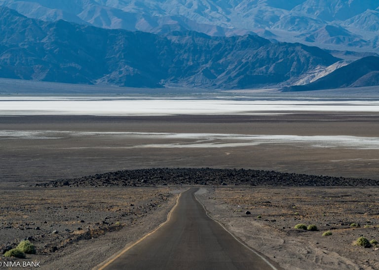 a hazy expanse of mountains intersected by a windy dirt road & salt basin in death valley california