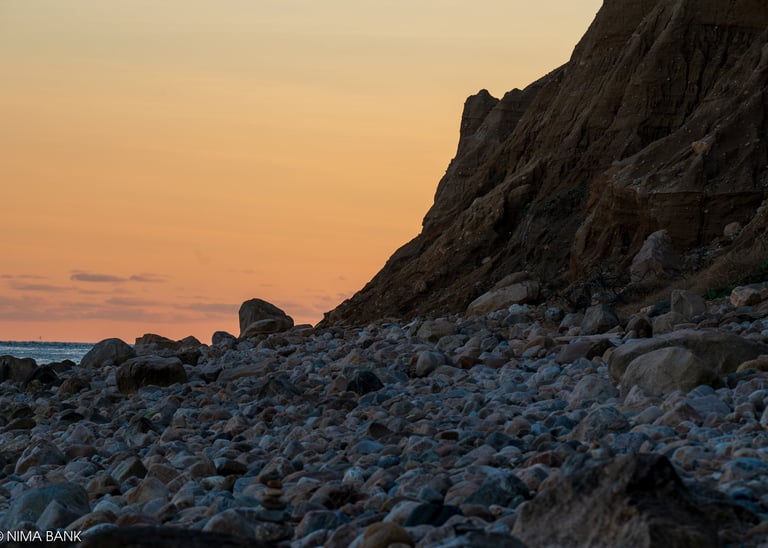 an orange sky at sunset on a rocky beach overlooking bluffs at montauk point