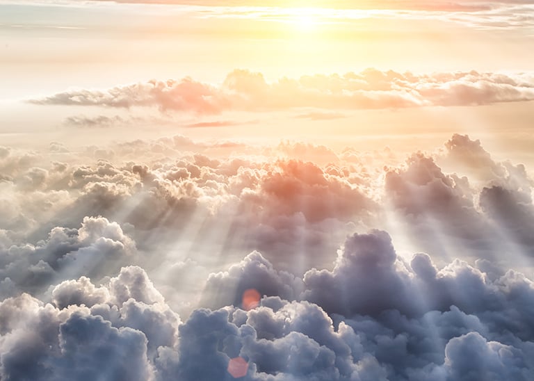 Photo of a group of clouds seen from above, with a heavenly light shining from afar