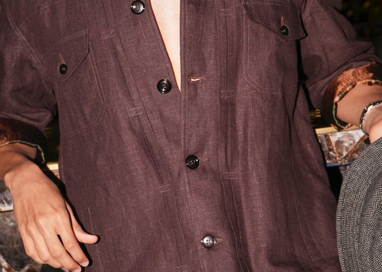 A man wearing a stylish brown linen button-down shirt with chest pockets and blue denim jeans.