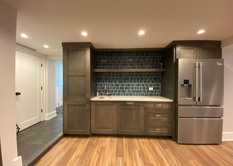 Basement wet bar with natural stone countertop, tile backsplash, and built-in storage cabinets