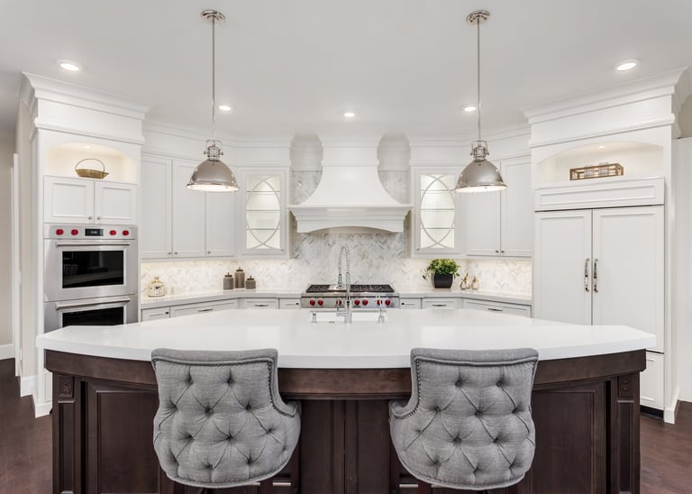 Modern luxury white kitchen featuring a large curved island, grey tufted bar stools, and pendant lights.