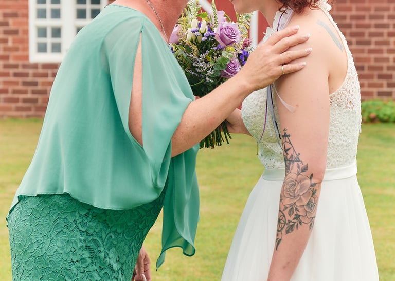 a woman in a wedding dress is kissed by her mother