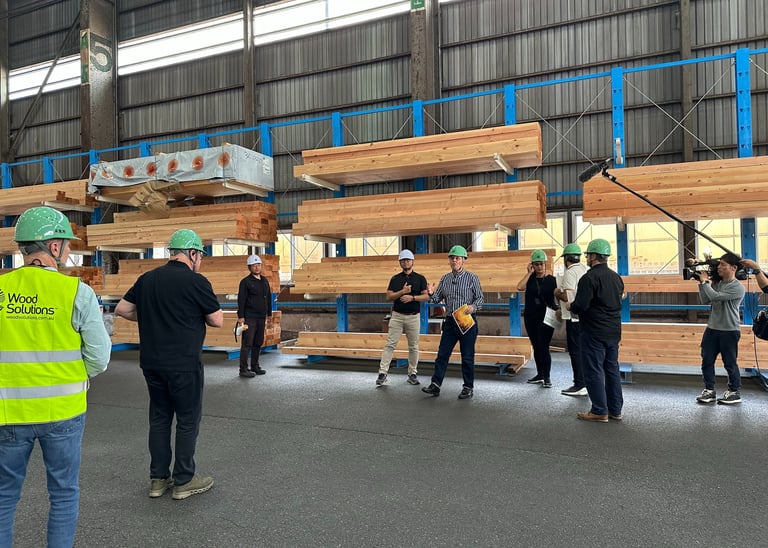 A group of engineers in hard hats film a site tour of a mass timber warehouse facility with glulam beams.