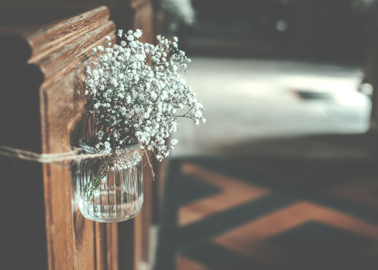 un vase avec des fleurs de gypsophile sur un banc d'église