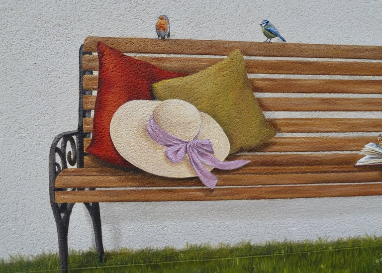 Détails d'une fresque peinte sur une façade. Tout est trompe-l'oeil: banc, oiseaux, herbe, livre,...