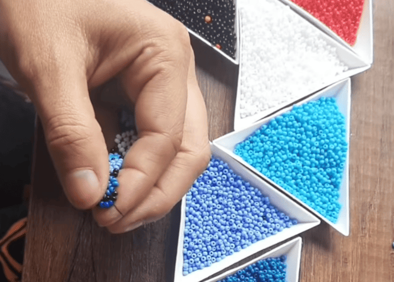 manos tejiendo una manilla con mostacillas azules