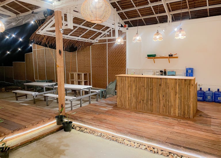 Rustic outdoor bar and seating area with bamboo accents, picnic tables, and warm pendant lighting.