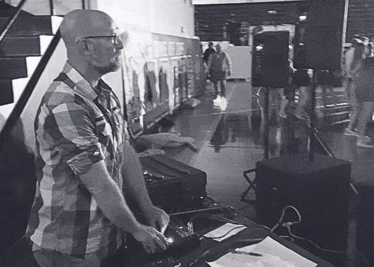 black and white image of man behind dj equipment