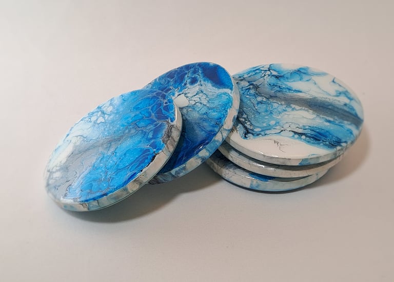 Handmade round coasters with blue and white fluid acrylic pour paint art in a marble design.