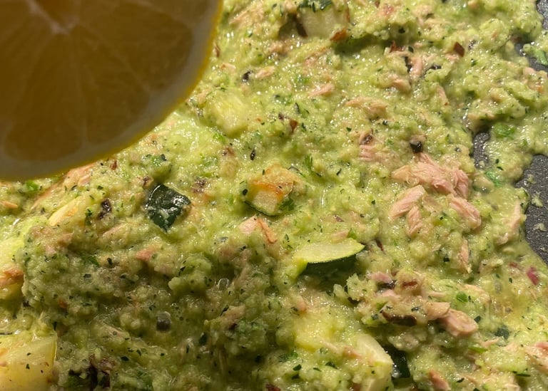 Fresh lemon juice being squeezed over a healthy green zucchini and tuna sauce cooking in a pan.