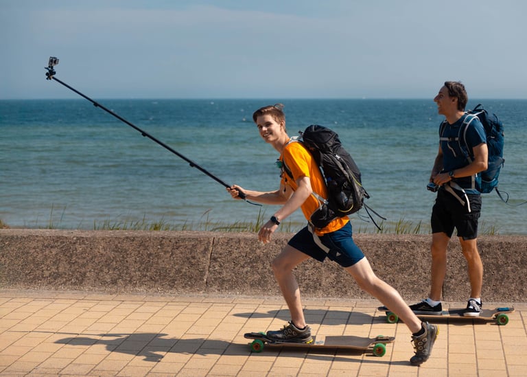 Zwei Männer fahren Longboard an der Küste mit Selfie-Stick. Lifestyle-Foto von Just Perspectives.